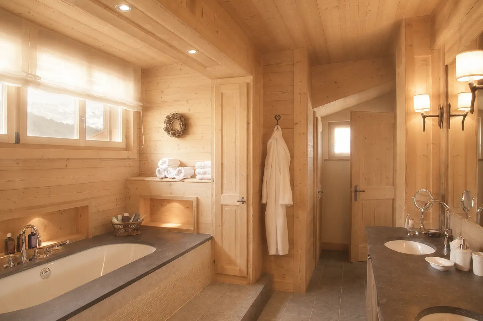 Full view of a stone-and-timber bathroom opening to soft alpine daylight